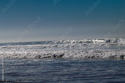 Clear blue skies and sunlight with Atlantic Ocean waves crashing onto sand beach with no people in Agadir, Morocco, Africa