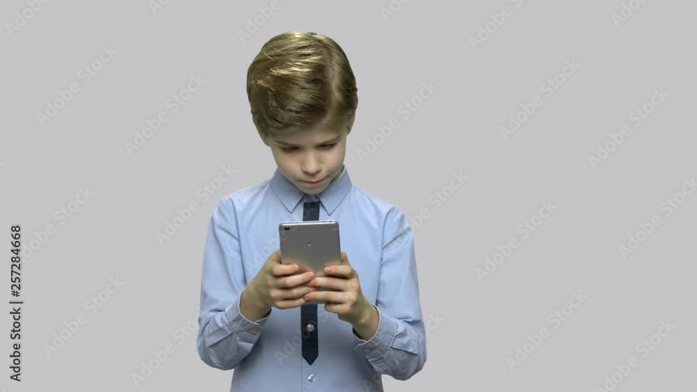 Kid boy surfing internet on smartphone. Little boy watching video on digital device against gray background. Children and modern technology. Kid boy surfing internet on smartphone. Little boy watching video on digital device against gray background. Children and modern technology.
