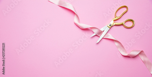 Grand opening. Gold scissors cutting pink satin ribbon, pink background