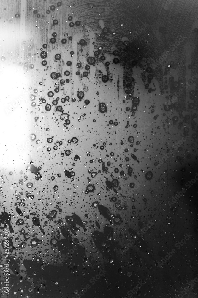 Closeup of condensation patterns on glass window, water droplets with light reflection and refraction, black and white abstract background Closeup of condensation patterns on glass window, water droplets with light reflection and refraction, black and white abstract background