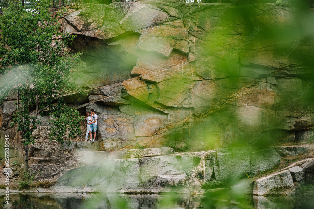 Fototapeta premium Young couple hugging a stone near the lake. A man and a woman stand against the background of the rocks. Top view. Nature. autumn. full length. looking at each other.