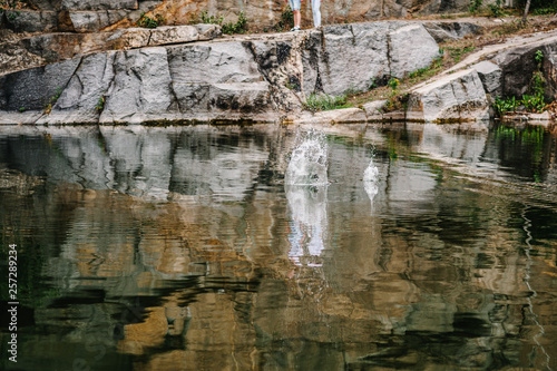 Splash of water from the fall of a stone into water. In the background are the legs of a woman and a man.