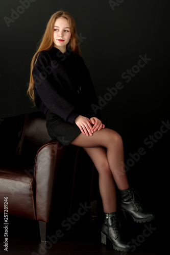 A teenage girl is sitting on a leather chair.
