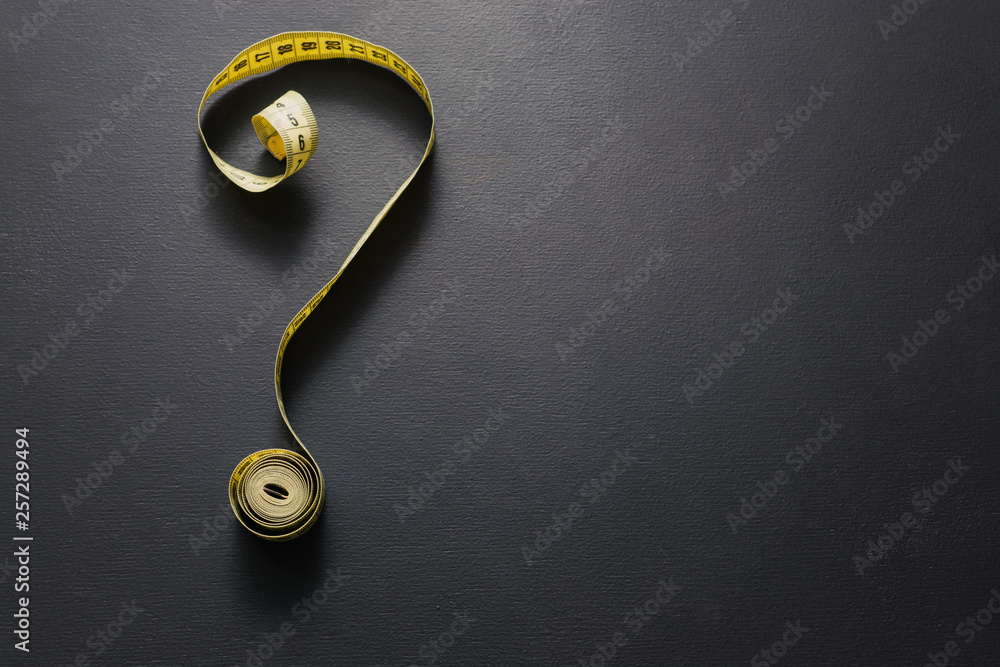 Tape measure forming the shape of question mark on chalkboard