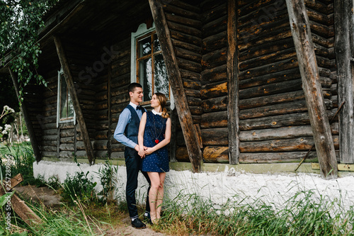 A man hugs back a tender woman. full length. looking at each other. on the background nature. Young lovers couple standing near an old wooden stylish house. © Serhii
