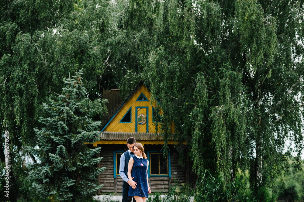 Φωτογραφία The young couple standing and hugging on the background a old wooden house on an island  near of trees