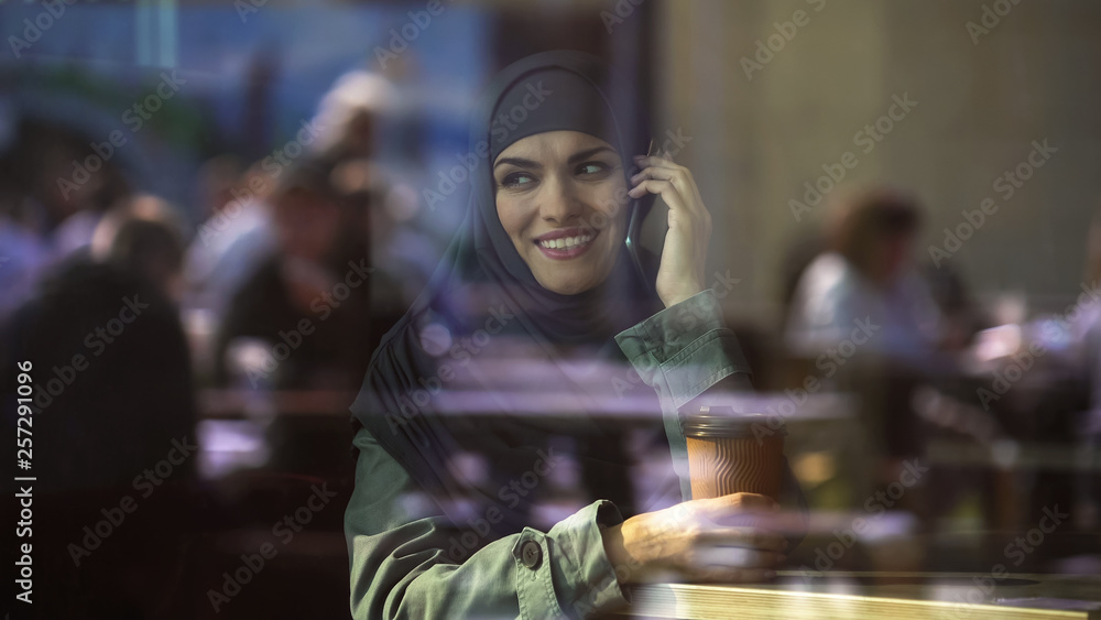 Attractive young Arab female talking on phone, spending free time in cafe, relax