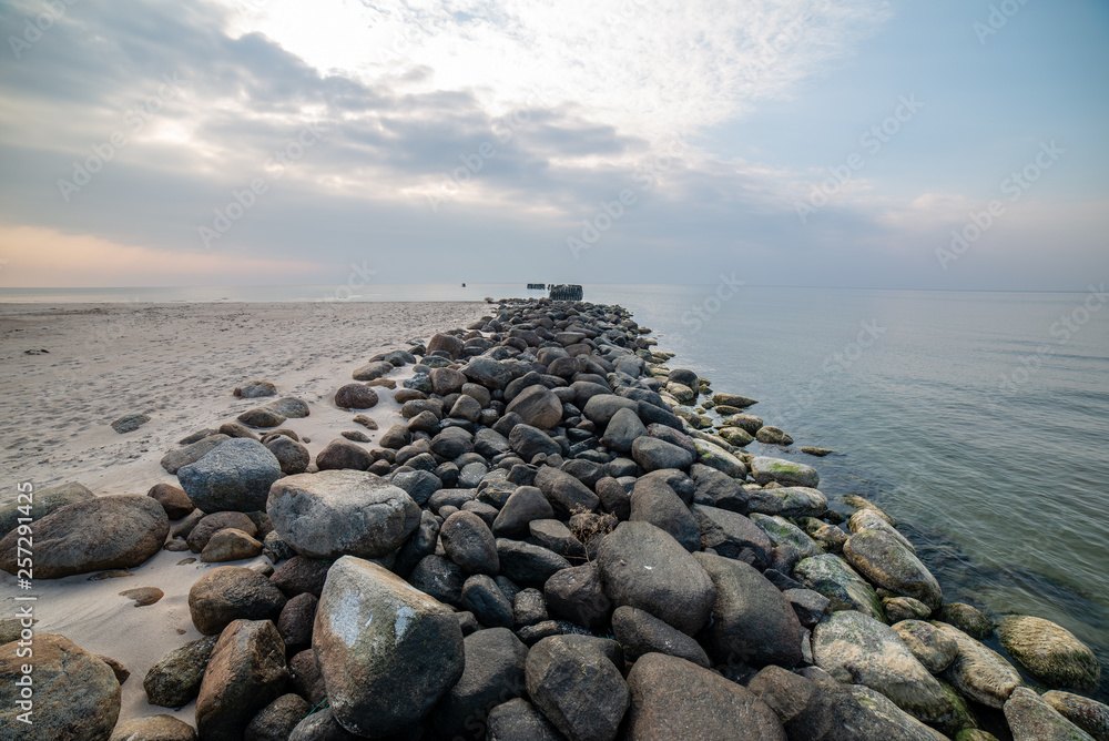 calm sea beach in summer with large rocks and wooden poles from old breakewater in the sea calm sea beach in summer with large rocks and wooden poles from old breakewater in the sea