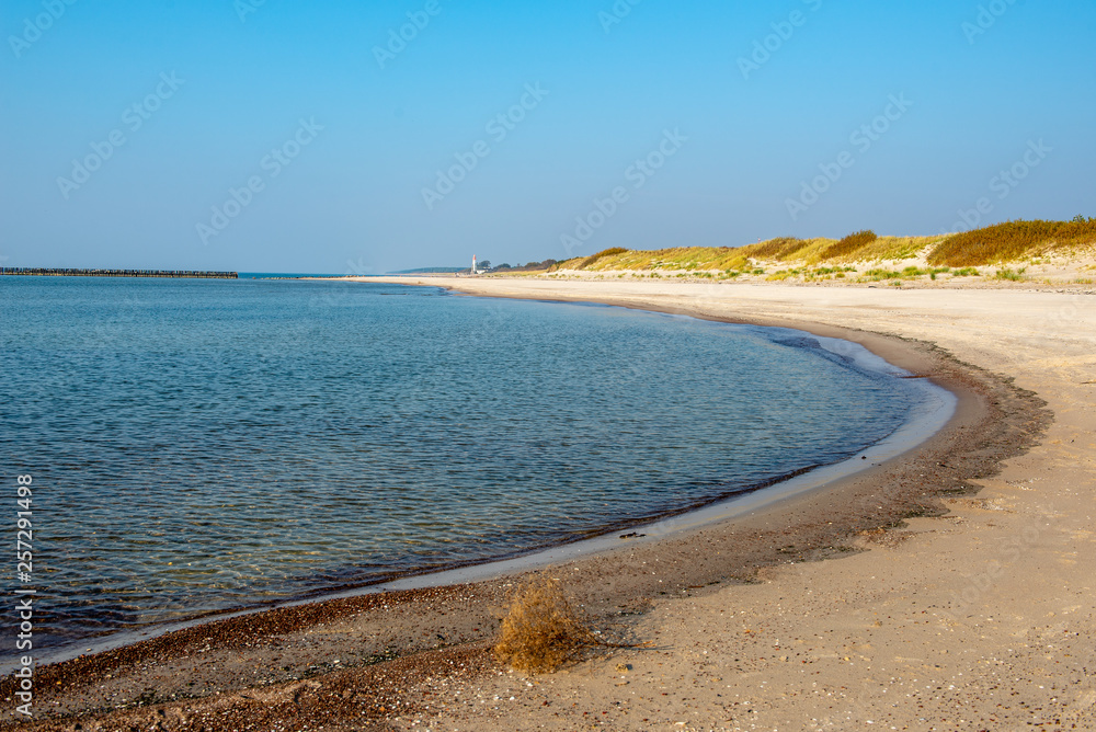 calm sea beach in summer with large rocks and wooden poles from old breakewater in the sea