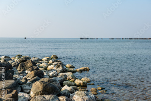 calm sea beach in summer with large rocks and wooden poles from old breakewater in the sea © Martins Vanags