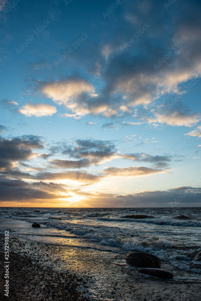 Fototapeta premium dramatic sunset over sea beach with rocks and stormy water