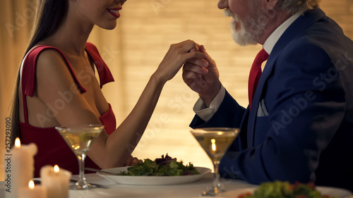 Senior gentleman holding hand of tender young wife, romantic date together photo