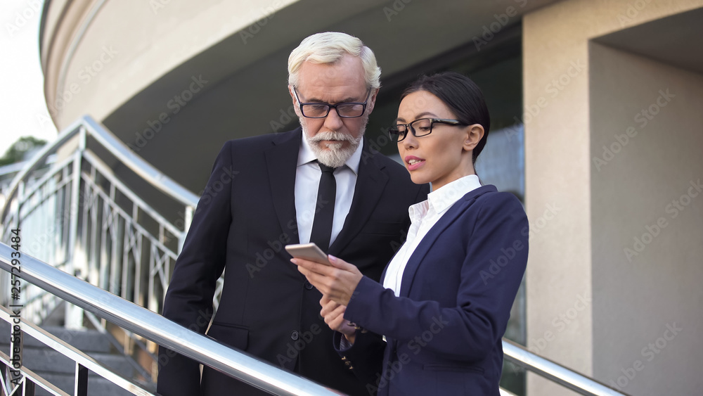 Old businessman watching meeting schedule in smartphone with young secretary Old businessman watching meeting schedule in smartphone with young secretary