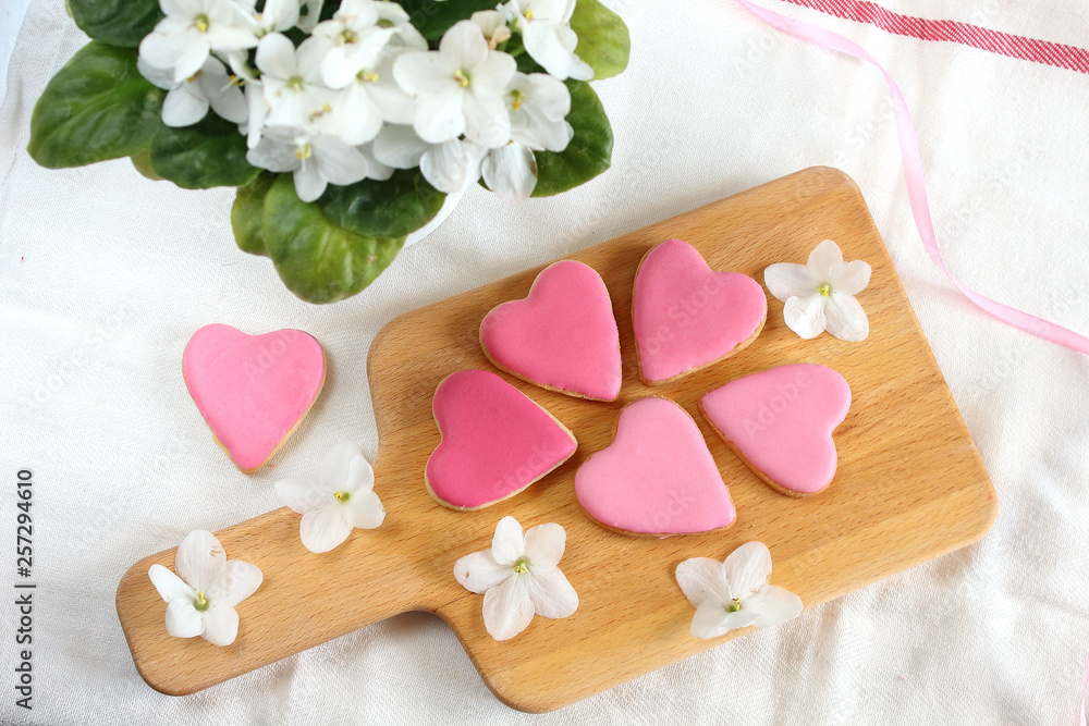 Pretty girlish flat style with gently pink hearts biscuits cookies with white violets blooming flowers and satin ribbon top view.14 february valentine's day gift treat Pretty girlish flat style with gently pink hearts biscuits cookies with white violets blooming flowers and satin ribbon top view.14 february valentine's day gift treat