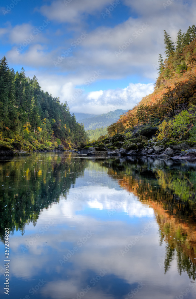 Nearly perfect fall reflections with blue sky and fluffy white clouds while rafting down the Rogue River in Oregon.
