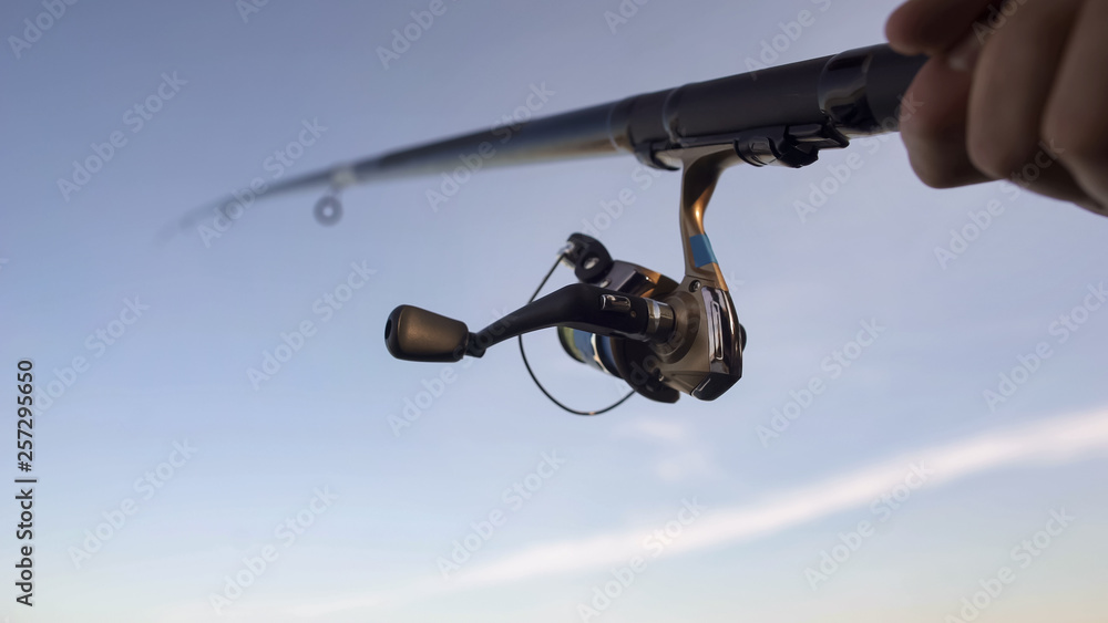 Close up of fishing reel, man catching fish with spinning rod in hand, gear Close up of fishing reel, man catching fish with spinning rod in hand, gear