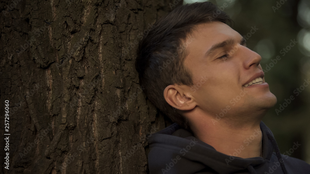Male leaning on tree trunk, loving nature, environmental protection and care Male leaning on tree trunk, loving nature, environmental protection and care