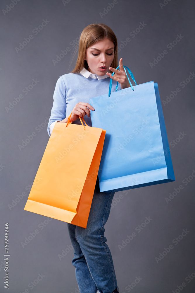 Fototapeta premium Emotional girl with colored bags standing on a gray background.