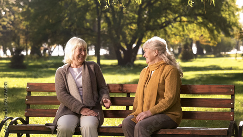 Two old fiends talking and laughing sitting on bench in park, retirement age