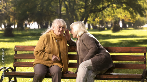 Old women telling secrets, sitting on bench in park, friendship, golden years