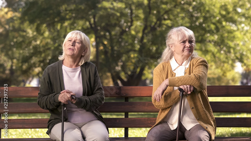 Mature ladies sitting separately on bench in park, friends argued and quarreled