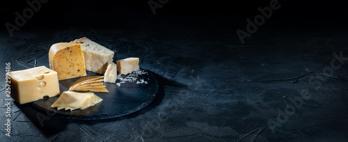 Different kinds of cheese on dark background, copy space