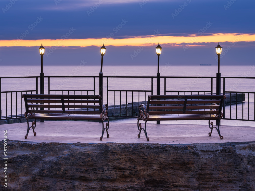 four street lighters and two benches on the pier in the morning twilight in Odessa in Ukraine