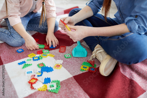 Close up portrait of two sisters playing with puzzles sitting on floor, copy space