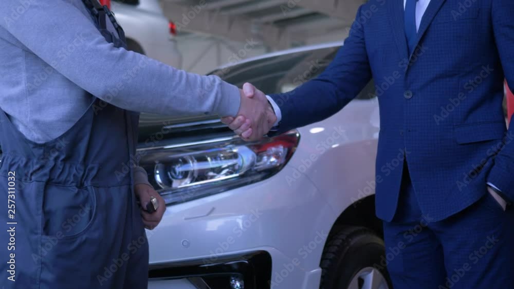 Auto business, customer man puts car keys in hands of auto mechanic for repair on service station on background of vehicle, close-up Auto business, customer man puts car keys in hands of auto mechanic for repair on service station on background of vehicle, close-up