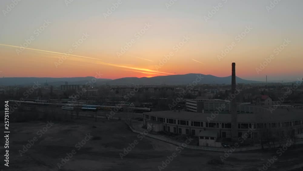 Wide aerial shot over an abandoned industrial area during sunset, closed factory