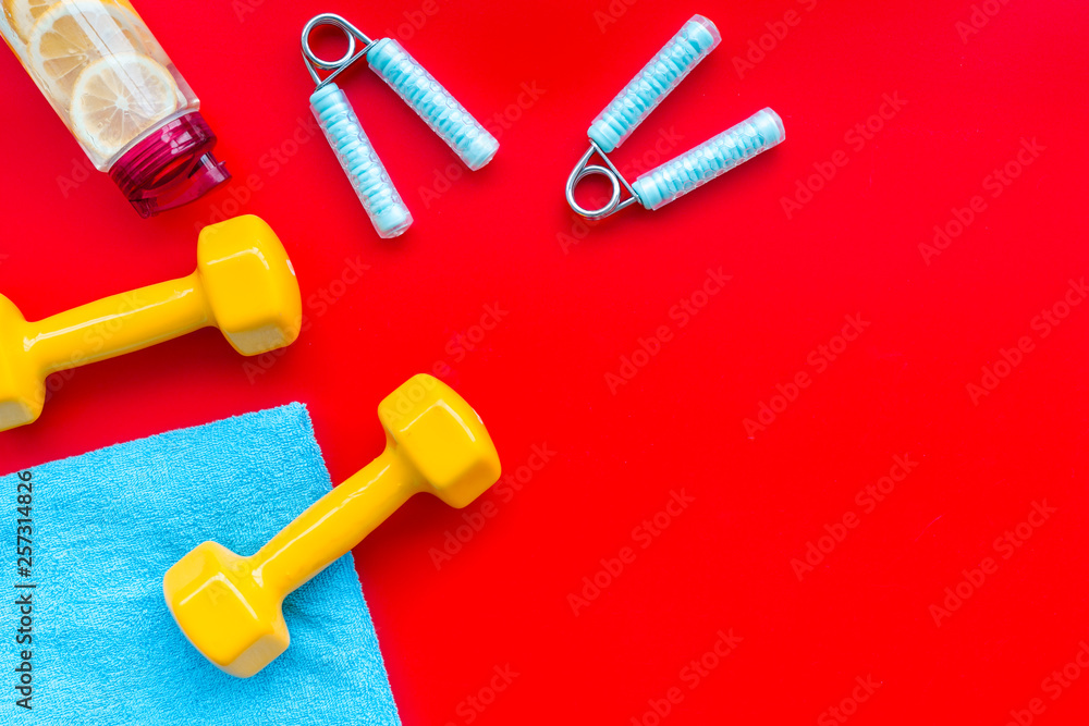 Fitness set with bars, towel, bottle of water and wrist builder on red background top view mock up Fitness set with bars, towel, bottle of water and wrist builder on red background top view mock up