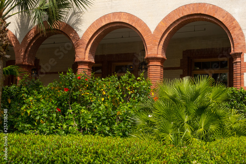 Brick archways against a stucco building with bushes in front