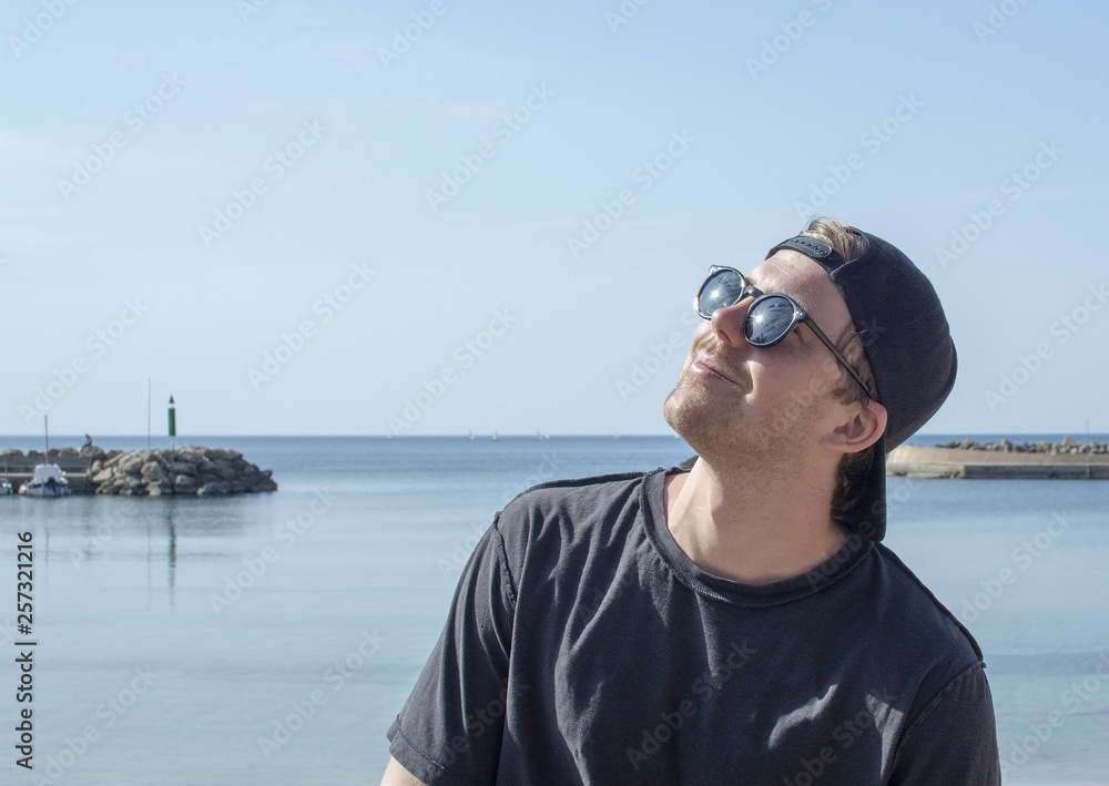 Young handsome happy man enjoys the sun in black glasses cap backwards