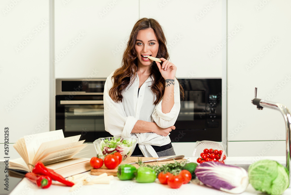 Brunette woman on the kitchen following book recipe and preparing healthy nutrition salad from fruits and vegetables. Housewife concept