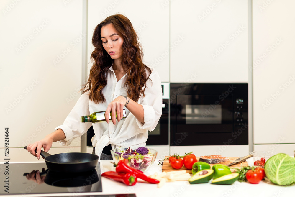 Brunette woman preparing fresh fish steak on the kitchen with vegetables and glass of white wine. Housewife concept