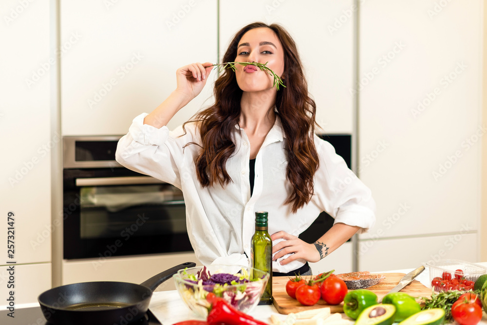 Brunette woman preparing fresh fish steak on the kitchen with vegetables and glass of white wine. Housewife concept