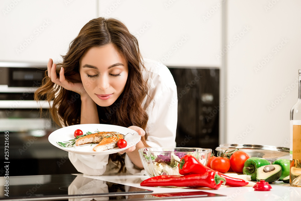 Brunette woman preparing fresh fish steak on the kitchen with vegetables and glass of white wine. Housewife concept Brunette woman preparing fresh fish steak on the kitchen with vegetables and glass of white wine. Housewife concept