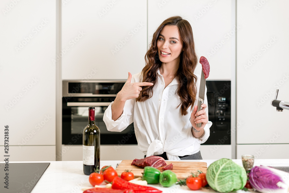 Brunette woman cooking and eating red meat steak with glass of red wine. Housewife concept Brunette woman cooking and eating red meat steak with glass of red wine. Housewife concept