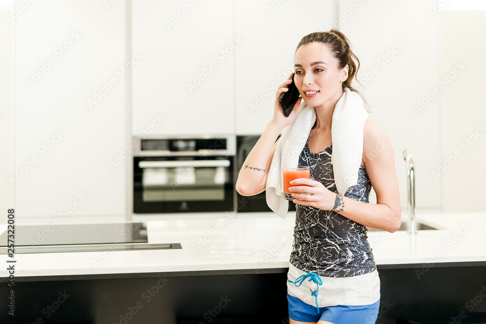 Attractive brunette girl with active fitness lifestyle training at home drinking glass of orange juice and using an app on the cellphone Attractive brunette girl with active fitness lifestyle training at home drinking glass of orange juice and using an app on the cellphone