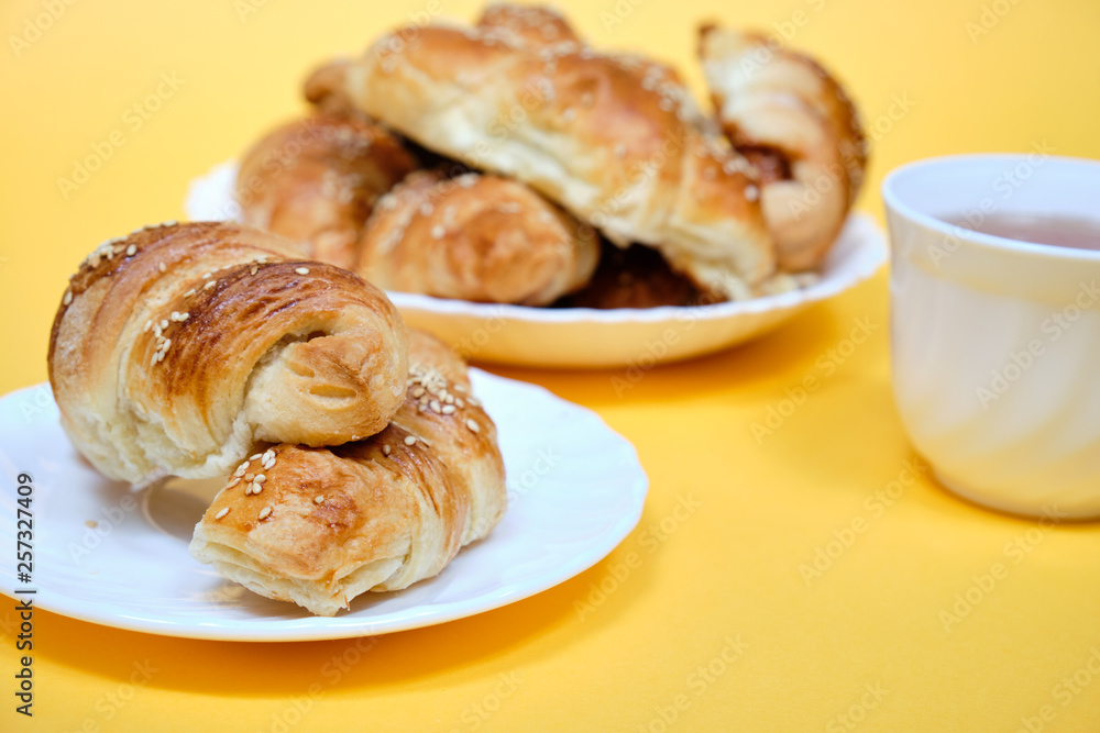 croissants on a white plate with a Cup of tea on a yellow background croissants on a white plate with a Cup of tea on a yellow background