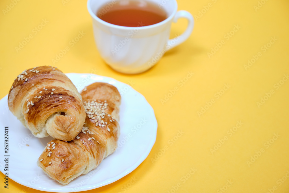 croissants on a white plate with a Cup of tea on a yellow background