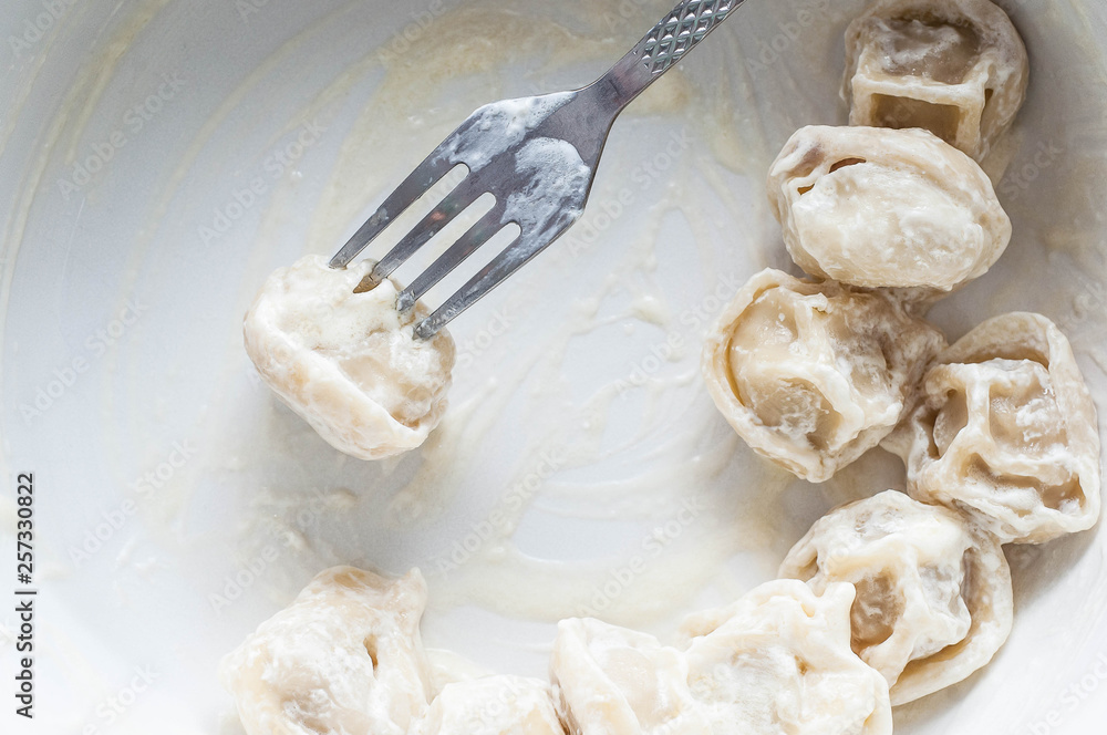 Fork with pork dumplings in sour cream sauce appetizing looks in a white plate with semi-finished Fork with pork dumplings in sour cream sauce appetizing looks in a white plate with semi-finished