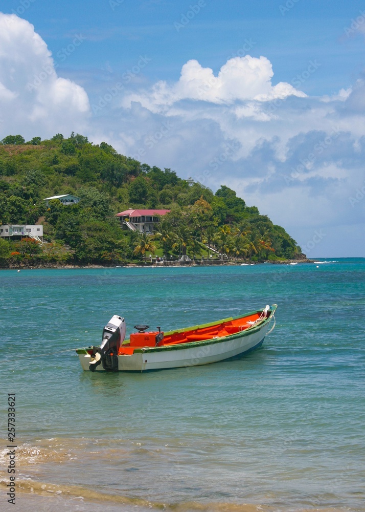 A traditional fishing boat with an outboard motor is anchored in the bay of a fishing village in a Caribbean island
