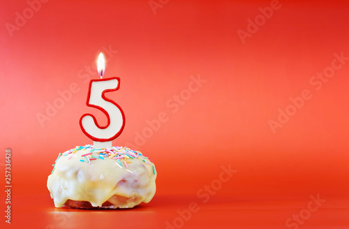 Five years birthday. Cupcake with white burning candle in the form of number 5. Vivid red background with copy space