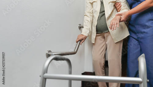 Elderly woman holding on handrail with caregiver photo