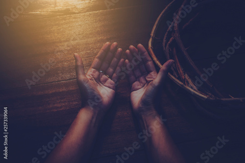 close up of woman hands prays near vine with thorns made like the crown of thorns of Jesus on wooden background  with light from above. Christian concept , Easter concept, copy space, vintage tone.