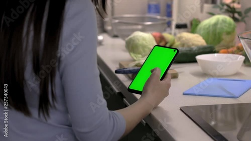 Young woman looking mobile app recipes for fresh salad on smartphone with chroma key green screen before cooking dinner, camera on slider