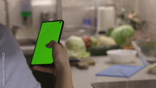 Girl looking mobile app recipes for fresh salad on smartphone with chroma key green screen before cooking dinner, camera on slider
