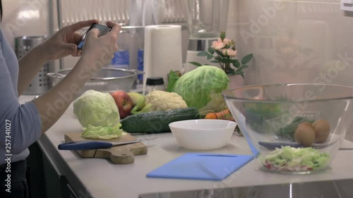 Woman taking photos of healthy salad preparation on smartphone at the kitchen, cooking application. Camera on slider