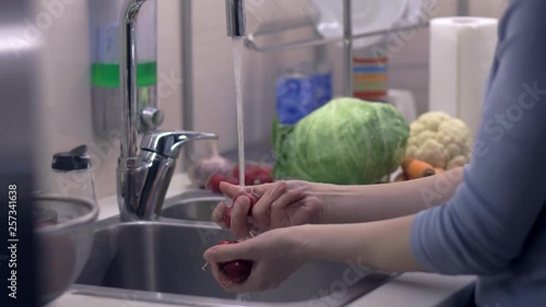 The young woman washes a radish to prepare healthy salad. Camera on slider